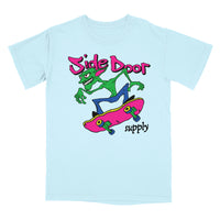 A light blue crewneck t-shirt featuring a colorful graphic of a green cartoon character riding a pink skateboard, with the text 'Side Door supply' in pink and black.